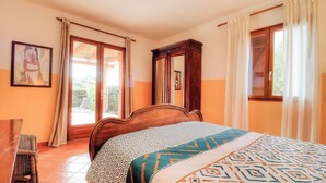 Una camera da letto con un letto, un armadio in legno, una sedia e una finestra con tende.