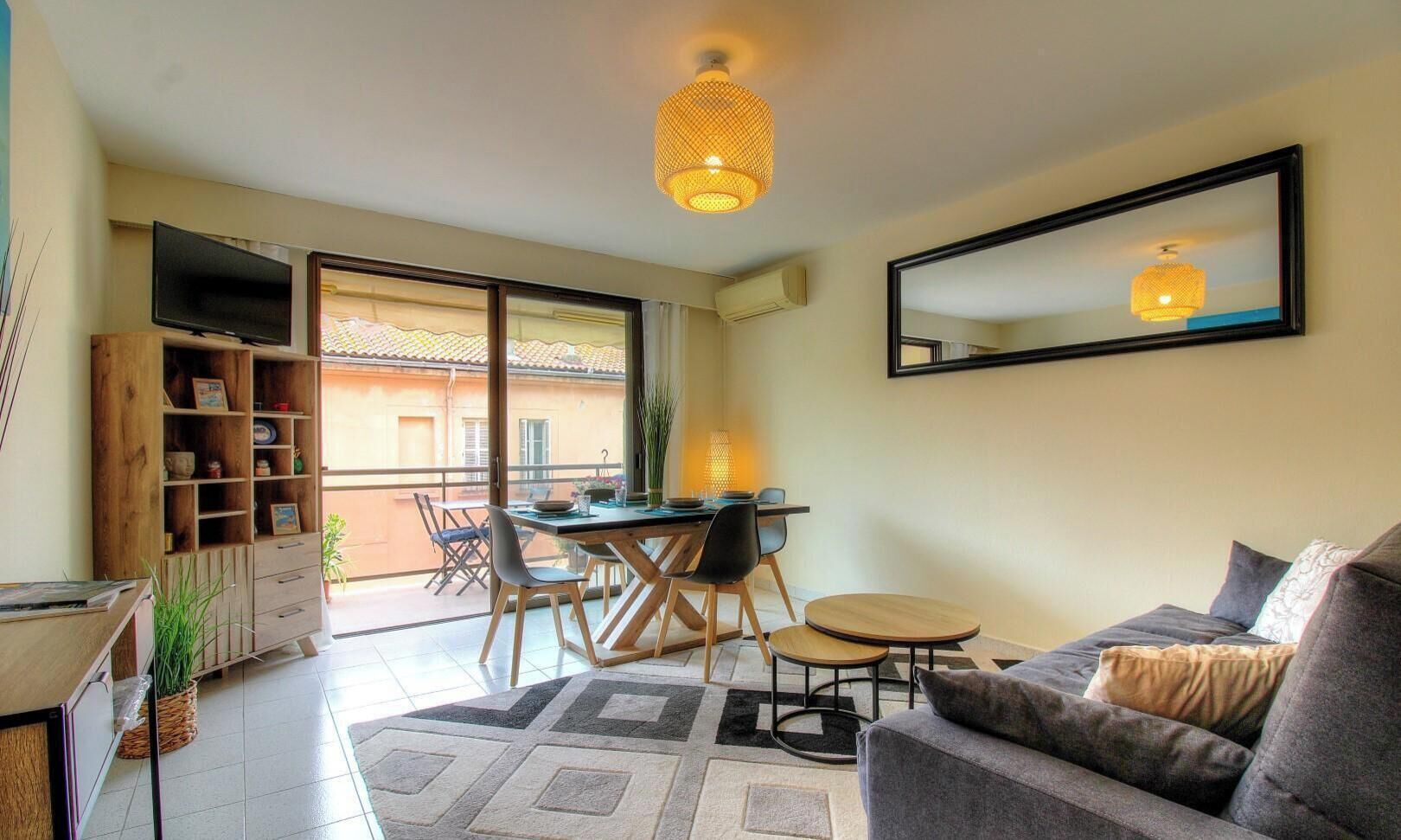 Una sala de estar con sofá, mesa de comedor, sillas, televisor, estantería y un ventanal grande.