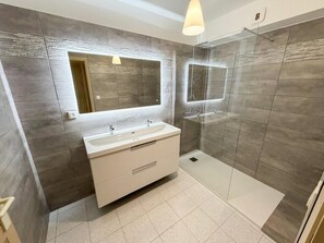 Ein modernes Badezimmer mit Waschtisch, großem Spiegel, Duschkabine und Toilette.
