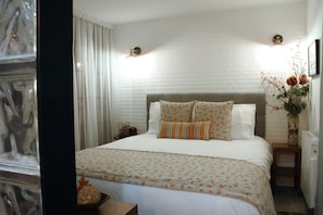 Een slaapkamer met een bed, een nachtkastje, een vaas met bloemen en een raam met gordijnen.