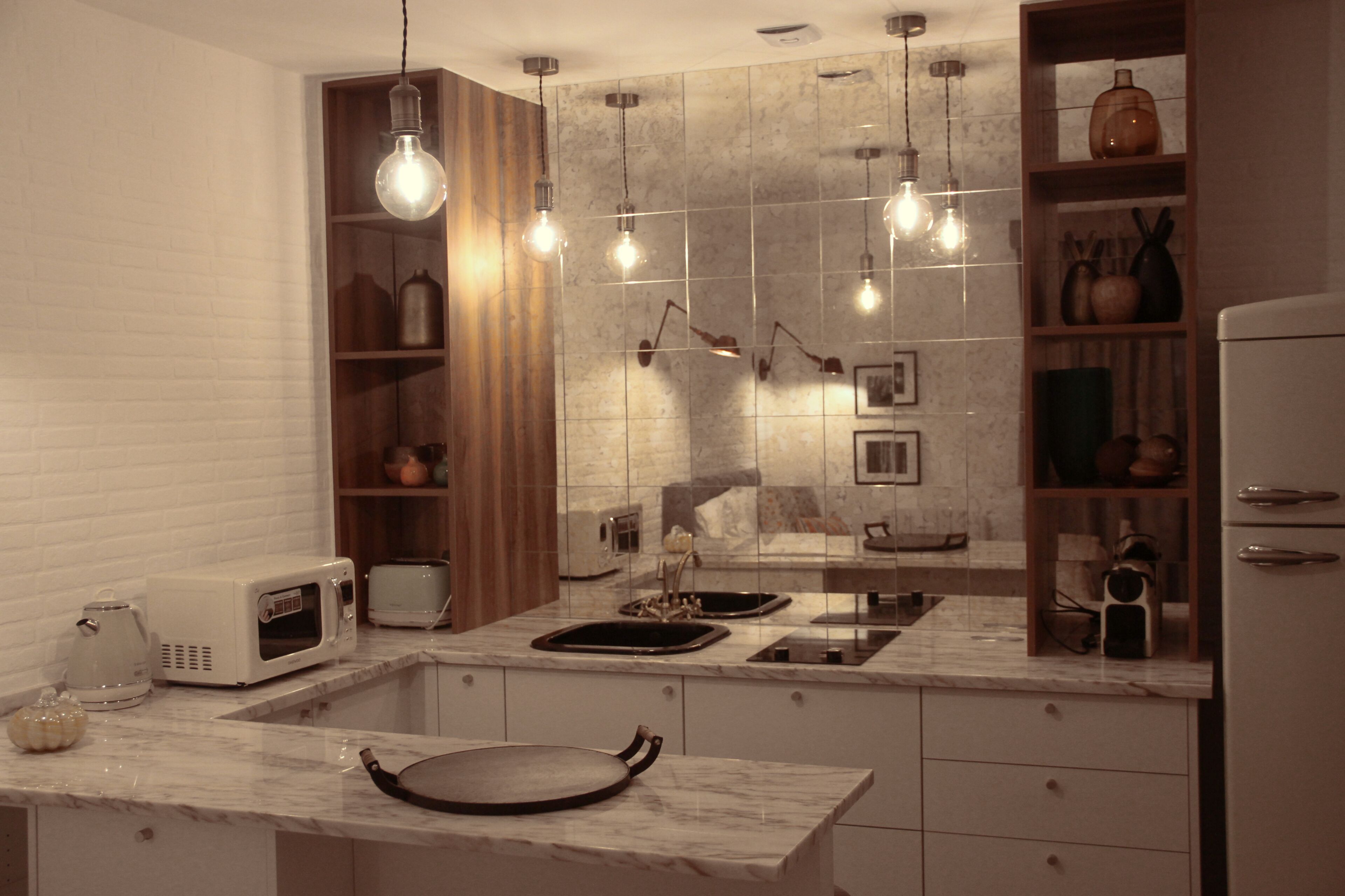 A modern kitchen with a marble countertop, built-in microwave, and a wooden shelf with kitchenware.
