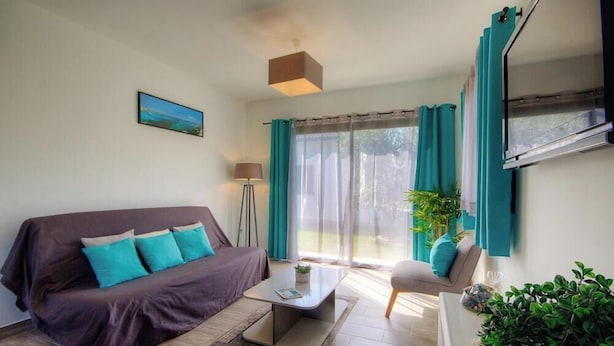 Un salon avec un canapé, une table basse, un fauteuil, une lampe et un téléviseur.