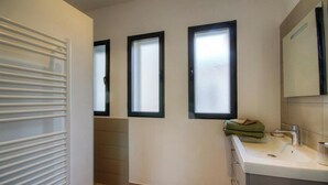Une salle de bain avec un lavabo blanc, un miroir et trois fenêtres à vitres dépolies.