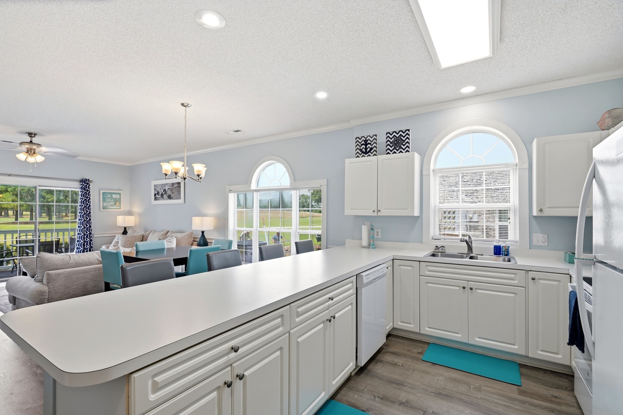 A modern kitchen with white cabinets, a large island, and a dining area with a view.