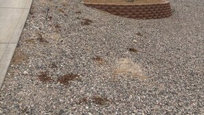 Zona residencial con entrada para vehículos, área de grava con jardinera de ladrillo y una casa con garaje.