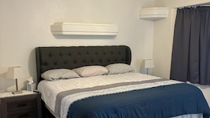 Un dormitorio con cama, mesitas de noche, ventilador de techo y ventana con cortinas.