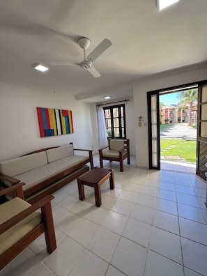 A living room with a sofa, chairs, a coffee table, a ceiling fan, and a view of a courtyard through a glass door.