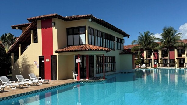 Ett hotell med en swimmingpool, en röd och gul byggnad och palmer.