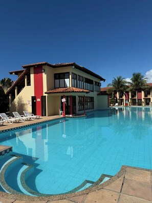 Un hotel con piscina, un edificio rojo y amarillo, y palmeras.