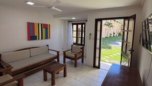 Ein Wohnzimmer mit einer Couch, Sesseln, einem Couchtisch, einem Fernsehschrank und einem Deckenventilator.