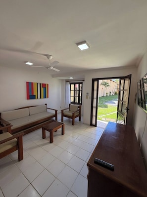 A living room with a sofa, chairs, a coffee table, a TV stand, and a ceiling fan.