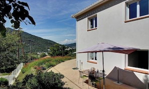 Ein Haus mit Terrasse, Tisch und Stühlen sowie einem großen Sonnenschirm.