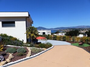 A modern house with a driveway, garden, and a view of a coastal town and mountains. - U Milvu - PIETROSELLA (PIETROSELLA)