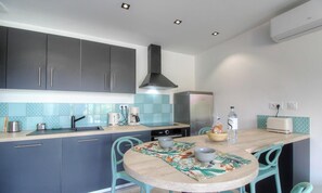 A compact kitchen with dark cabinets, a stainless steel refrigerator, a coffee maker, and a table with a floral placemat. - U Milvu - PIETROSELLA (PIETROSELLA)