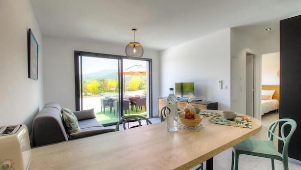 Une cuisine moderne avec un plan de travail en bois, un coin repas comprenant une table et des chaises, un canapé et une grande fenêtre donnant sur l’extérieur.