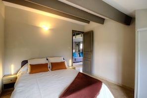 Ein Schlafzimmer mit Bett, Nachttischen, einer Tür und Blick in einen weiteren Raum.