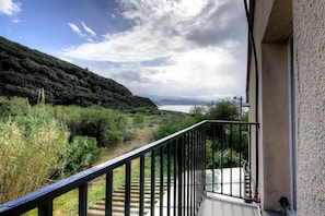Ein Balkon mit Blick auf eine Küstenlandschaft, eine Treppe und ein Gebäude mit strukturierter Fassade.