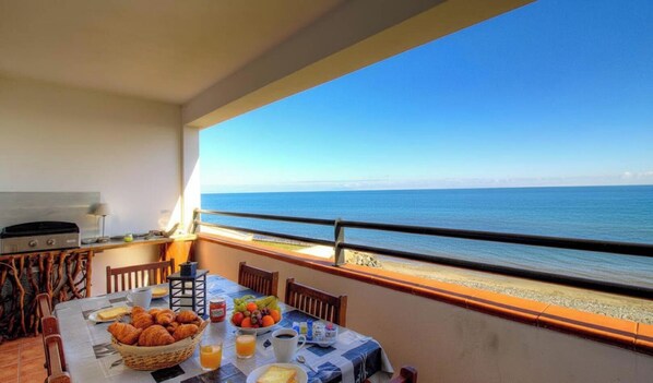Ein Balkon mit Frühstückstisch, mit Blick auf einen Strand.