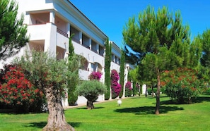 Ein Hotel mit heller Fassade, mehreren Balkonen und einem gepflegten Garten mit verschiedenen Sträuchern und Bäumen.