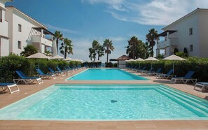 Ein Pool mit Liegestühlen und Sonnenschirmen, umgeben von Gebäuden und Palmen.