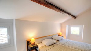 A bedroom with a bed, two bedside lamps, a window, and a wooden ceiling beam. - A Torra - AITI - Gîte (AITI)