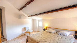 A bedroom with a large bed, a chair, a nightstand with a lamp, and a wooden ceiling beam. - A Torra - AITI - Gîte (AITI)