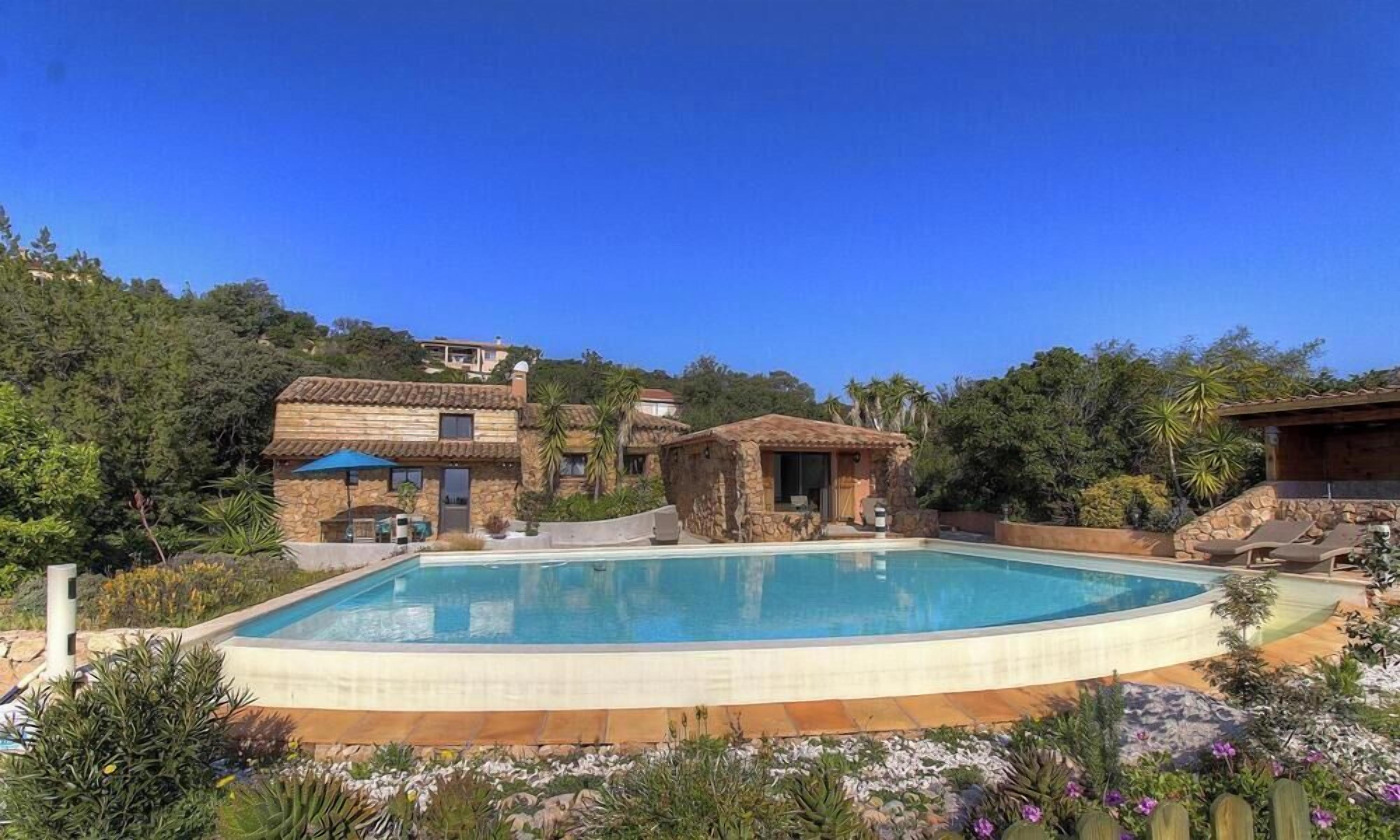 A swimming pool surrounded by stone buildings, a clear sky, and lush greenery.