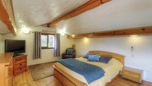 Ein Schlafzimmer mit einem Bett, einem Fernseher, einem Sessel, einer Kommode und einem Fenster.