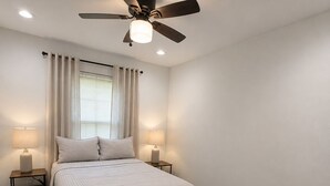 A bedroom with a bed, two bedside tables, a ceiling fan, and a window with curtains. -  Spacious 4-bedroom Houston Retreat Near NASA, Downtown & Galveston Cruises (Houston)