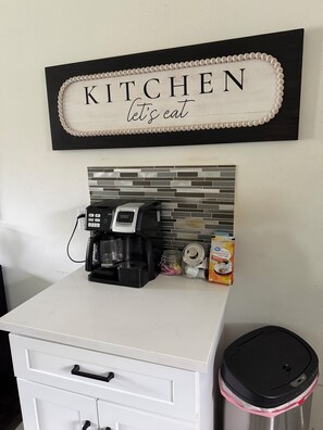 A kitchen counter with a coffee maker, a box of coffee, and a trash can. -  Spacious 4-bedroom Houston Retreat Near NASA, Downtown & Galveston Cruises (Houston)