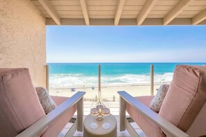 A balcony with two chairs and a small table, overlooking a beach with clear blue water and a sandy shore. - Oceanfront Solana Beach 2 BDR Condo (Solana Beach)
