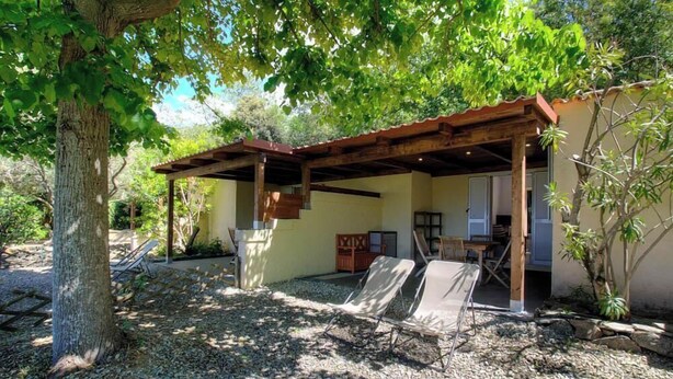Ein überdachter Außenbereich mit Stühlen, einer Holzpergola und einem Gebäude mit Tür und Fenstern.