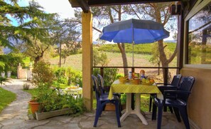 Eine überdachte Terrasse mit Tisch für zwei, Stühlen und einem blauen Sonnenschirm.