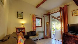 Ein Wohnzimmer mit einer Couch, einem Fernseher, einem Bücherregal und einer Glasschiebetür, die zu einem Außenbereich führt.