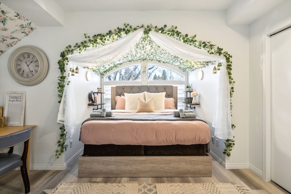 Un dormitorio con cama con dosel, un reloj, una mesita de noche y vistas a árboles.