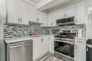 Una cocina moderna con armarios de madera clara, una estufa de acero inoxidable, un microondas y un lavavajillas.
