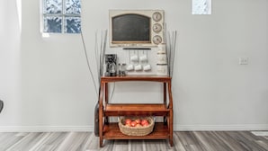 A wooden coffee table with a basket of apples, a coffee maker, and a clock with city names. - Central 3BR Home | Sleeps 8, 4 Beds + 2 Bathrooms (Calgary)