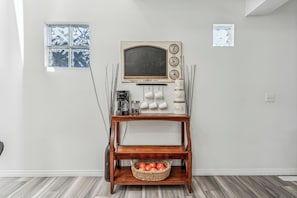 Una mesa de centro de madera con una cesta de manzanas, una cafetera y un reloj con nombres de ciudades.