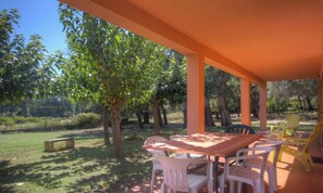Eine Terrasse im Freien mit Tisch und Stühlen, umgeben von Bäumen und Grünpflanzen.