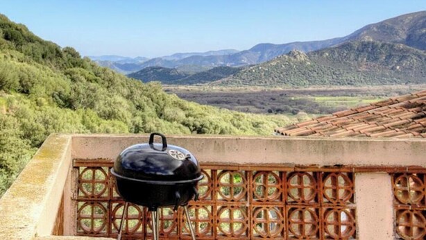 Een barbecue op een balkon met uitzicht op een bergachtig landschap.