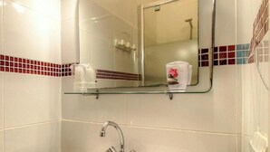 Een badkamer met een wit wastafelmeubel, een spiegel en een glazen plank met toiletartikelen.