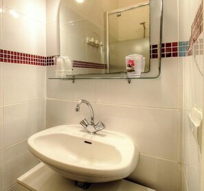 Ein Badezimmer mit einem weißen Waschbecken, einem Spiegel und einer Glasablage für Toilettenartikel.