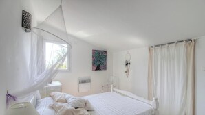 Ein Schlafzimmer mit einem Bett, einem Nachttisch, einer Lampe, einer Wand-Klimaanlage, einem Traumfänger und einem Baumgemälde.