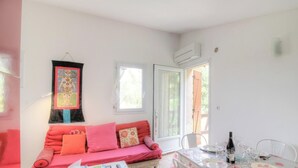 Ein Zimmer mit einer Couch, einem Esstisch mit Stühlen, einem Fenster und einer Klimaanlage.