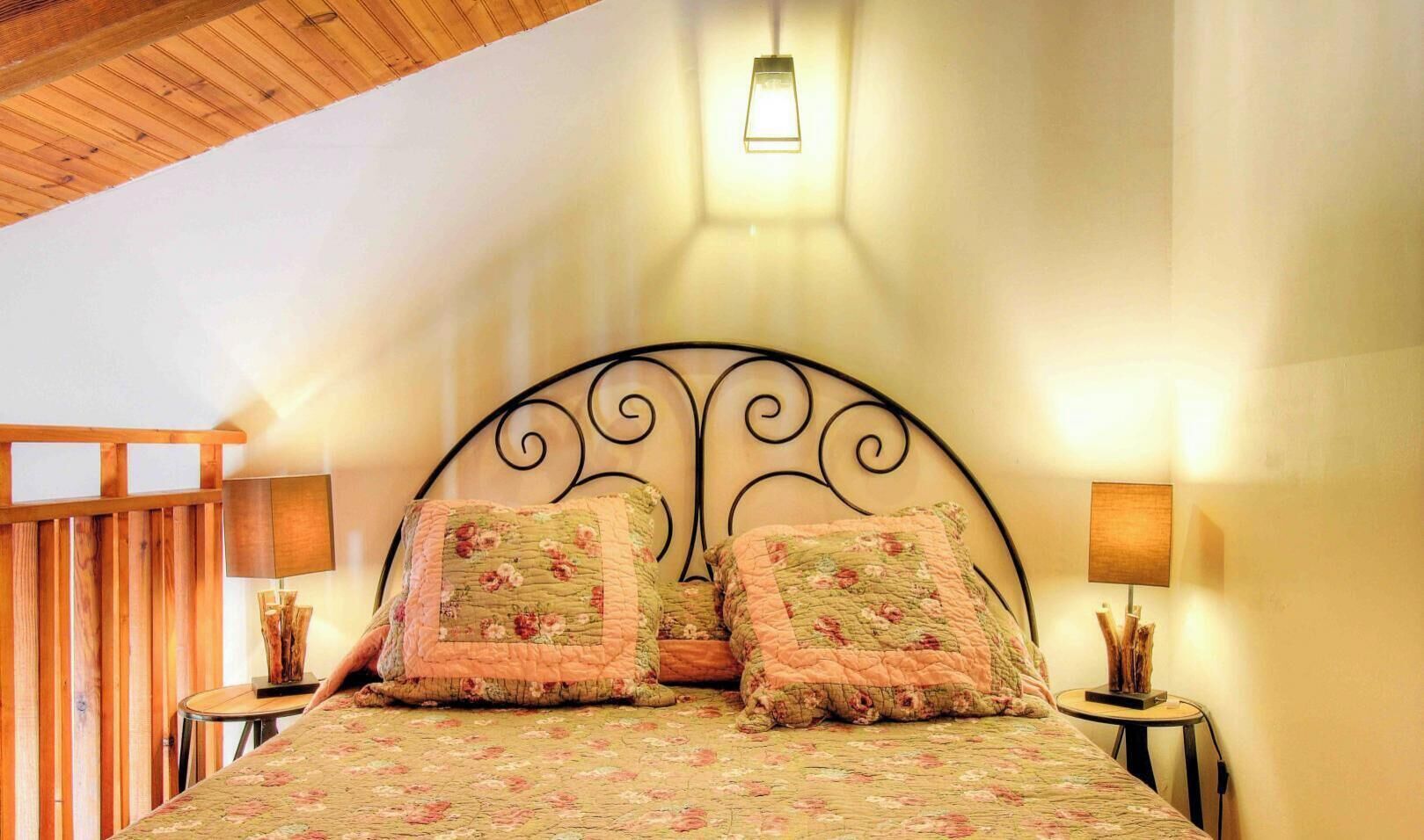 Une chambre à coucher comprenant un lit, deux oreillers, deux tables de chevet, une lampe fixée au mur et un mur avec des lambris en bois.