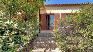 A building with a tiled roof, a set of stone steps leading to a wooden door, and lush greenery surrounding the entrance. - ORTIGLIESI - SERRA DI FERRO (SERRA DI FERRO)