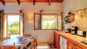A kitchen with wooden cabinets, a dining table with chairs, a window with a view of greenery, and a coffee maker on the counter. - ORTIGLIESI - SERRA DI FERRO (SERRA DI FERRO)