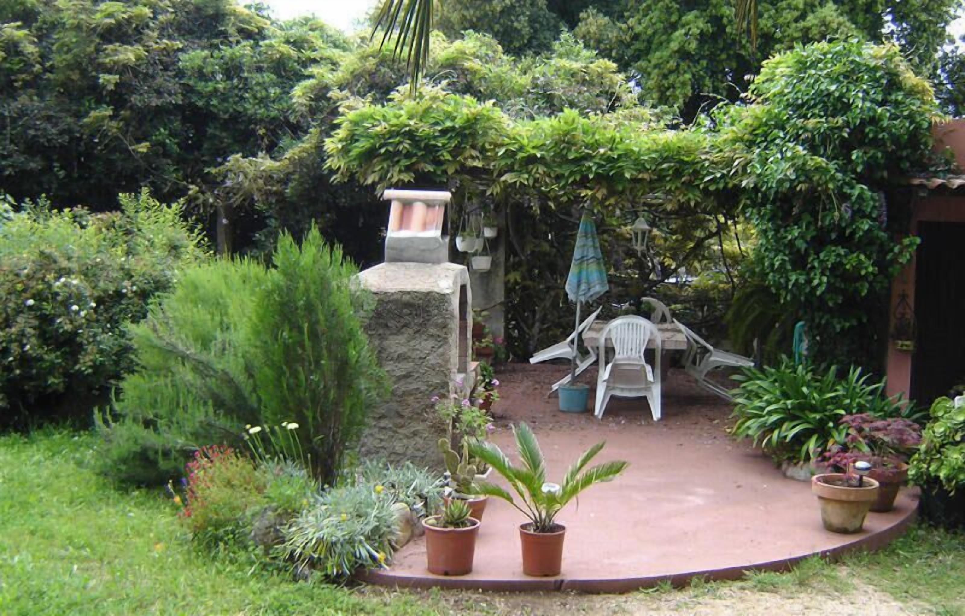 A garden patio with a stone structure, a white chair, a table, and various potted plants.