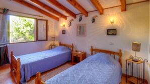 Ein Zimmer mit zwei Holzbetten, einem Fenster mit Blick auf Grünflächen, einem Spiegel, Wandleuchten und einem kleinen Tisch mit Lampe.