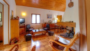 Ein gemütliches Wohnzimmer mit Holzboden, einem Fernseher, einem Esstisch und verschiedenen Stühlen.